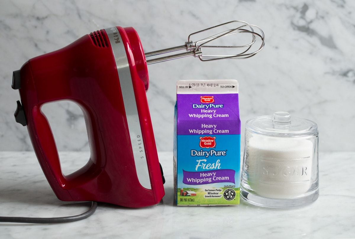 How to Make Homemade Whipped Cream Whipped cream sugar and an electric hand mixer on a marble surface