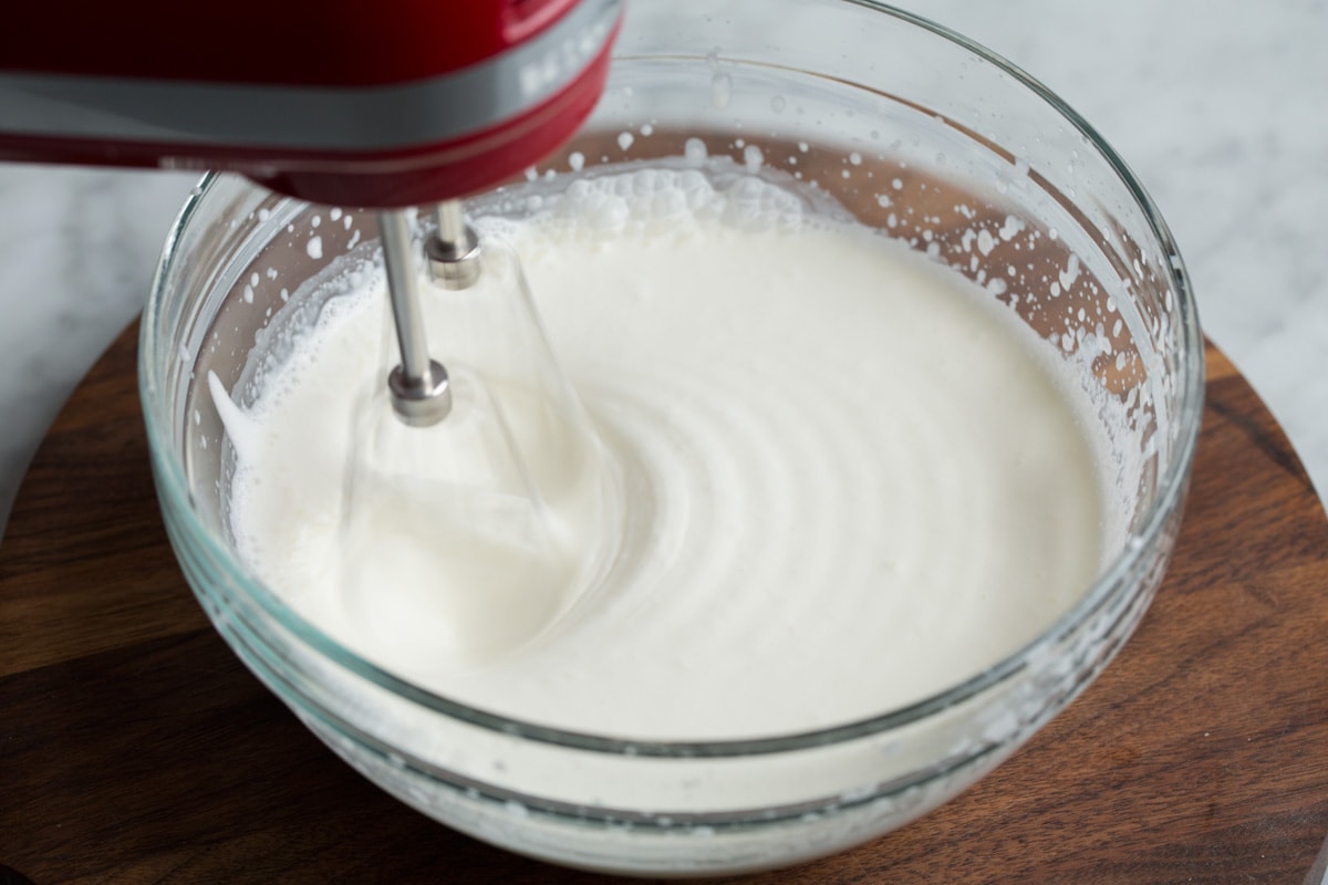 Whipped Cream Showing how to make whipped cream. Mixing heavy cream and sugar in a glass mixing bowl using an electric hand mixer until thickened.