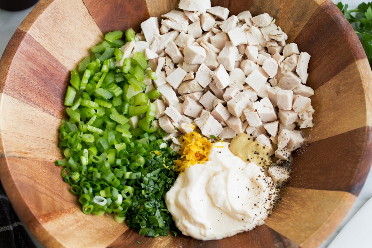 The Best Chicken Salad! Showing how to make chicken salad, tossing chicken breast pieces, mayonnaise, dijon, lemon, celery, green onion, parsley in a wooden mixing bowl.