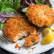 Two salmon patties on a white serving plate with a side of salad.
