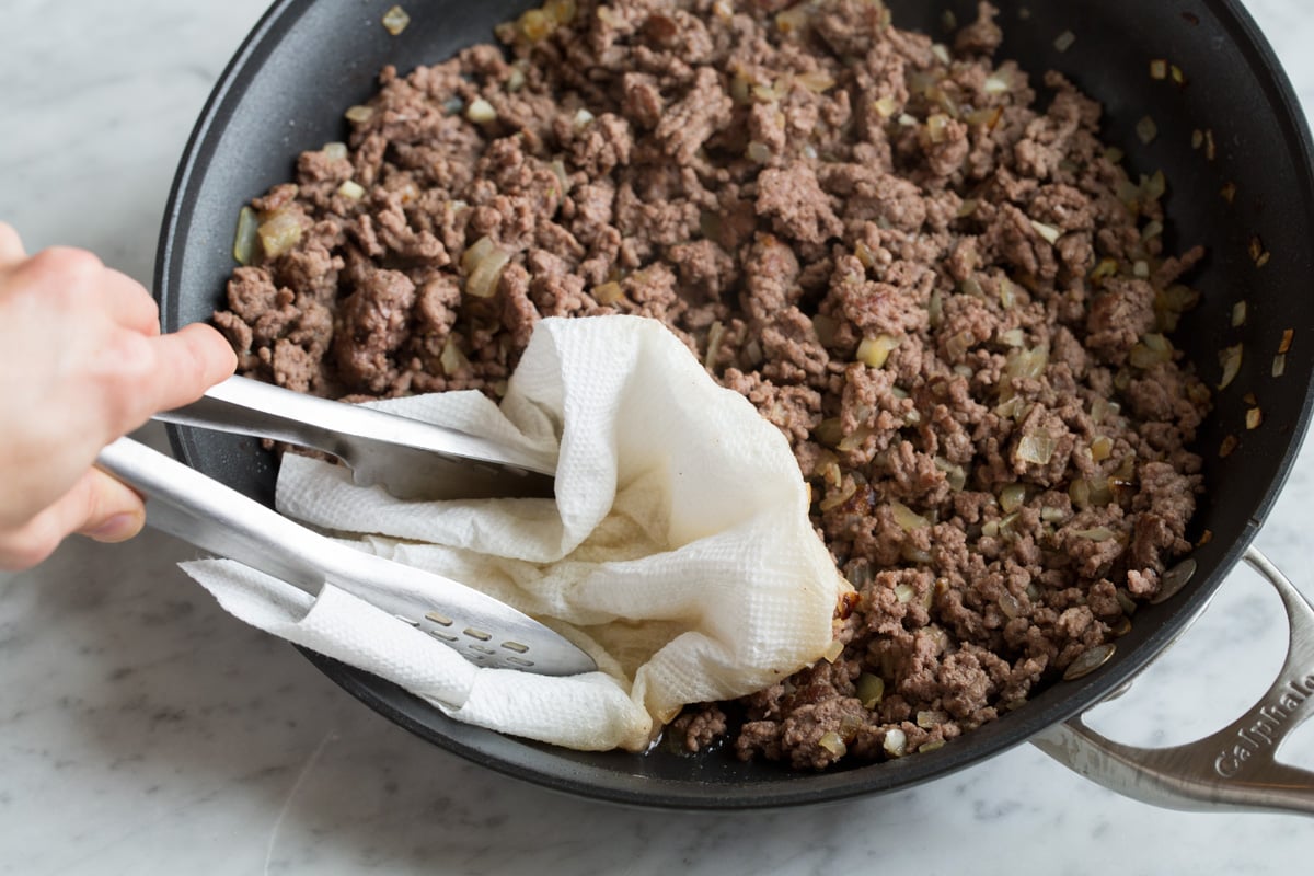 Stuffed Peppers Draining fat from ground beef in skillet using a paper towel and tongs.