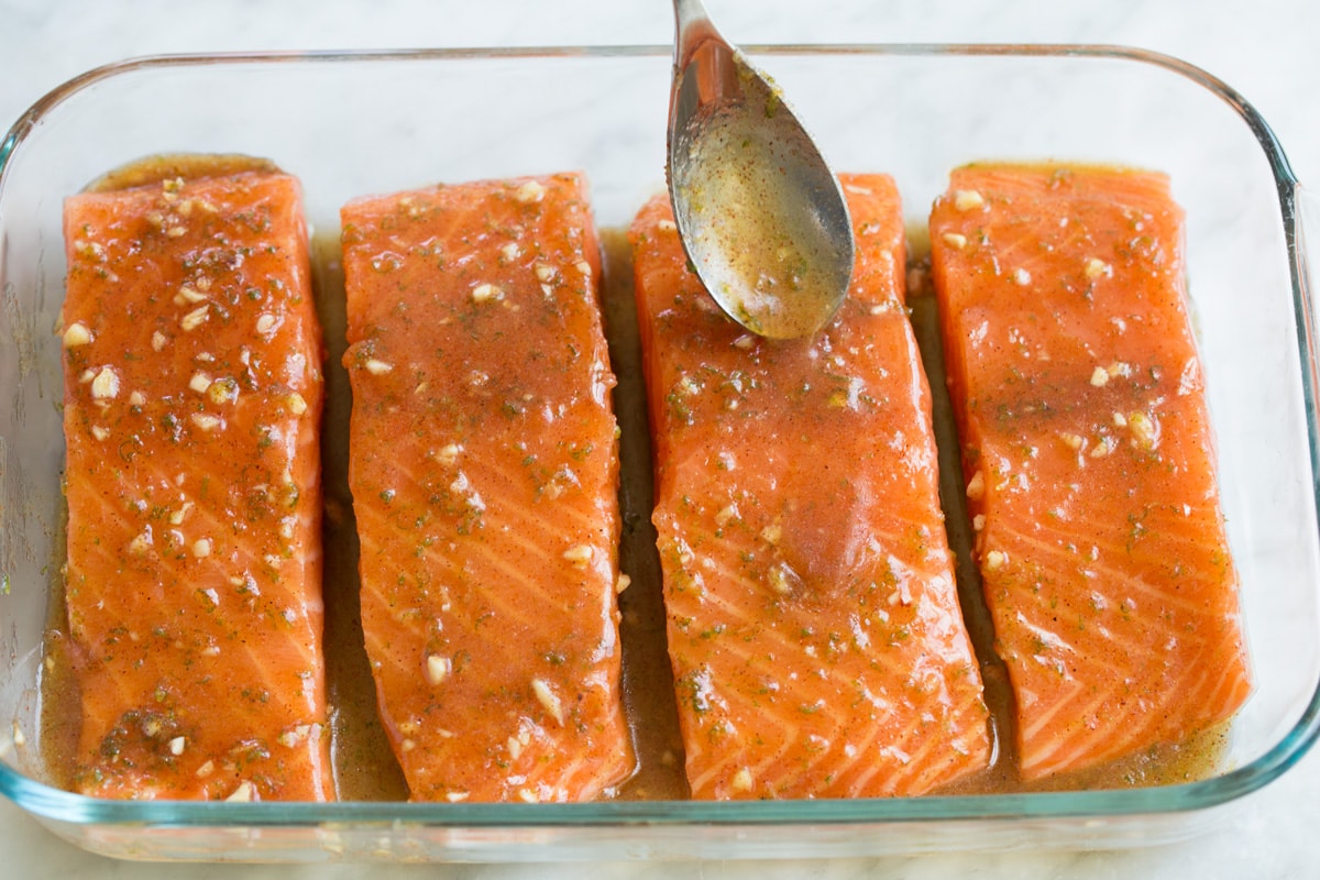 Brown Sugar Lime Baked Salmon Spooning sauce over salmon fillets in a small glass baking dish.