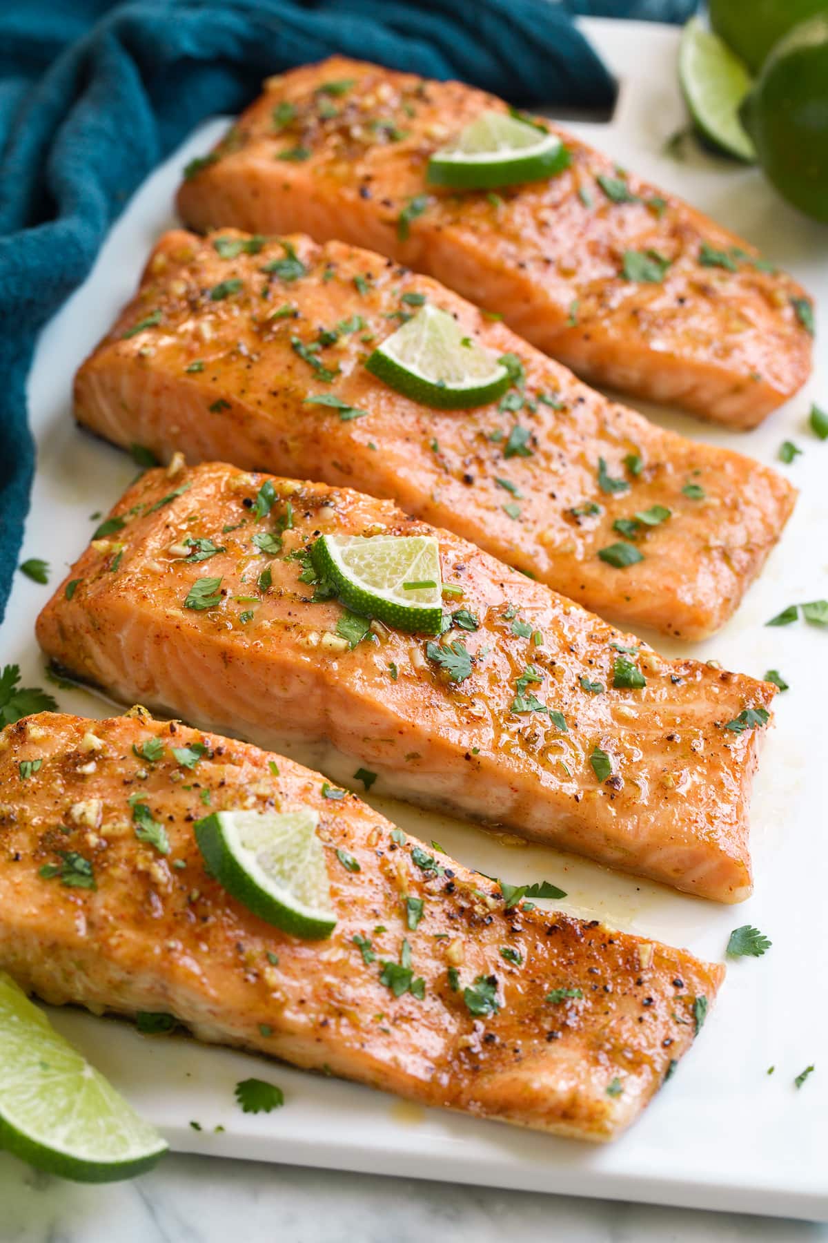 Baked salmon on a white serving platter. It's topped with a brown sugar and lime sauce and garnished with limes and cilantro.