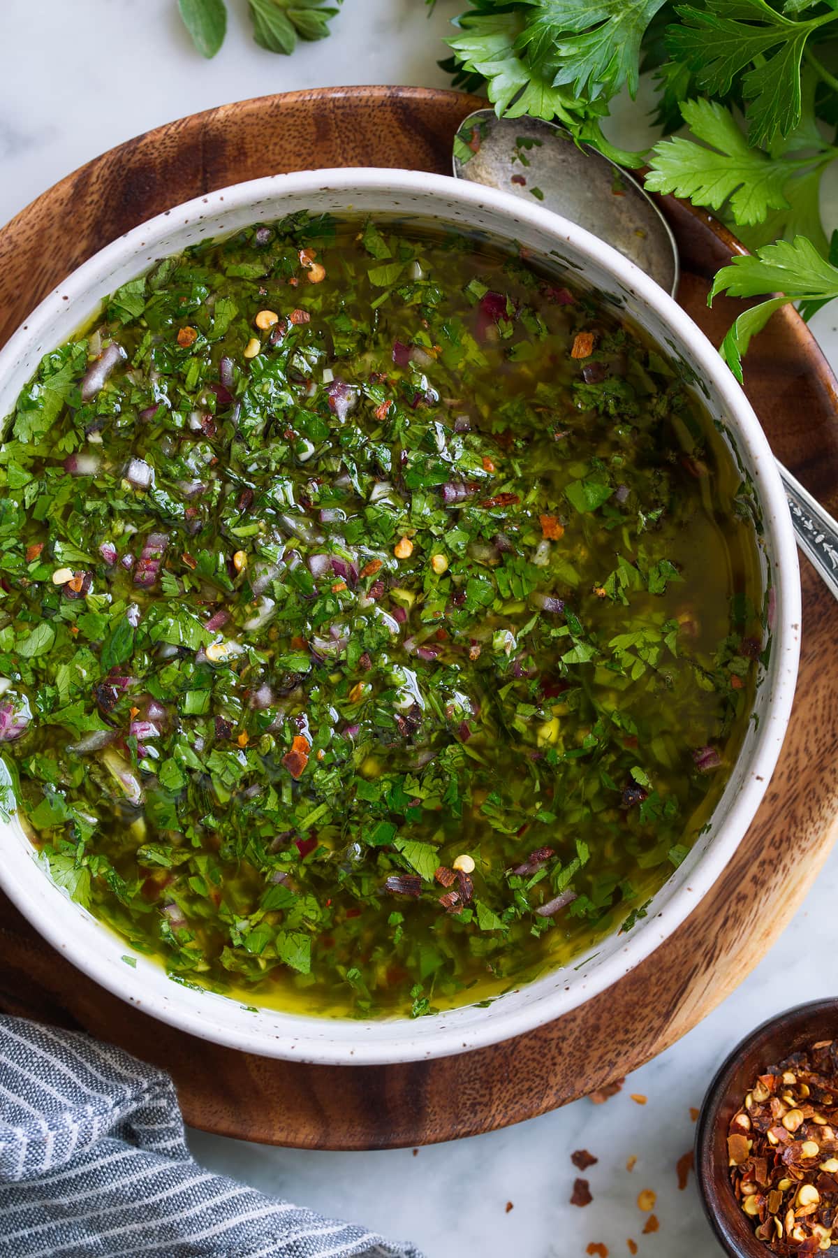 Best Chimichurri Sauce Overhead close up image of chimichurri in a bowl set over a wooden plate on a marble surface.
