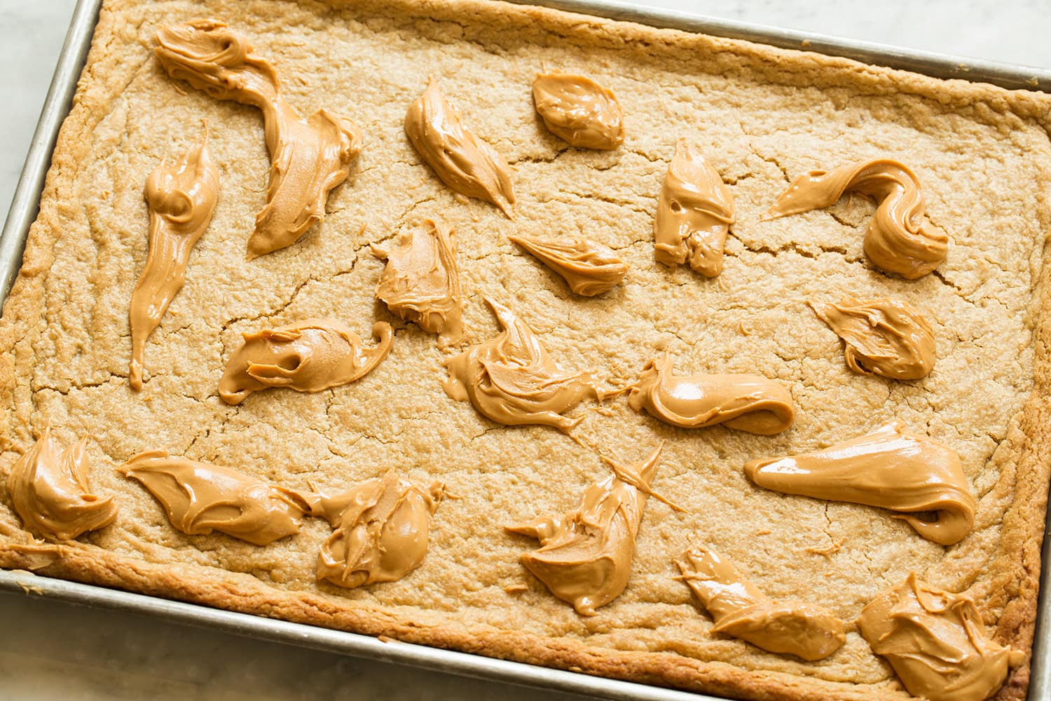 Peanut Butter Bars Spoonfuls of peanut butter spread over sheet of baked cookie bars.