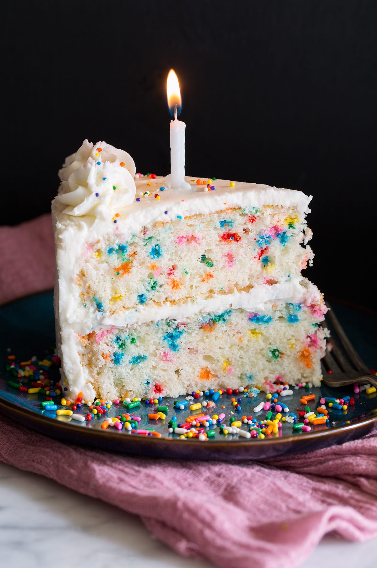 Birthday Cake - the perfect funfetti sprinkled cake! It's perfectly soft and fluffy and amazingly delicious! My kids absolute favorite cake! #cake #birthdaycake #dessert #birthday Slice of birthday cake with multi color dots in cake and topped with buttercream frosting and a birthday. candle.