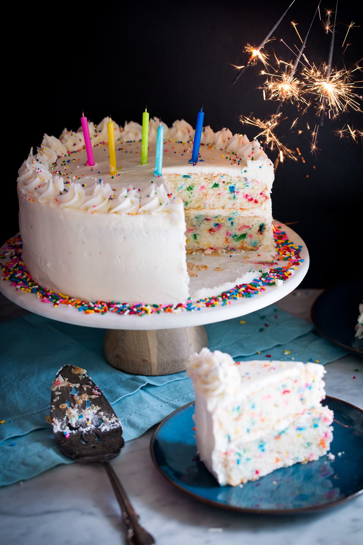 Birthday Cake - the perfect funfetti sprinkled cake! It's perfectly soft and fluffy and amazingly delicious! My kids absolute favorite cake! #cake #birthdaycake #dessert #birthday Birthday cake topped with candles and sparklers to the side.