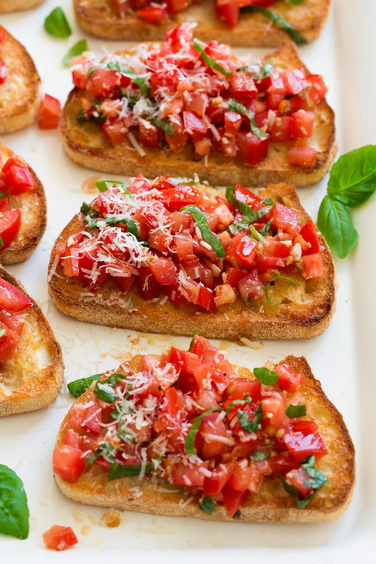 Bruschetta Recipe - perfect every time and so easy to make! An Italian staple! #bruschetta #tomatoes #basil #bread #sidedish Bruschetta with toasted bread and fresh tomato basil mixture on top, set on a white serving platter.