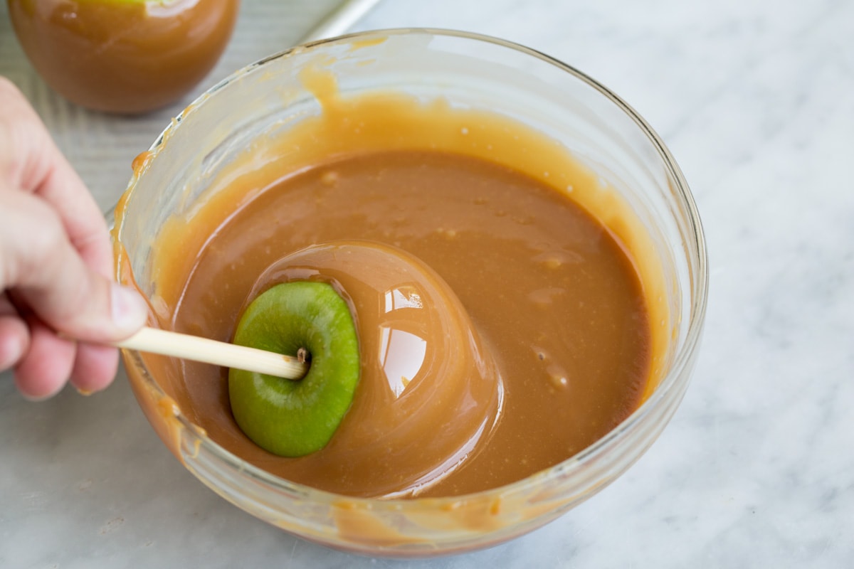 Easy Caramel Apples Rolling granny smith apple on stick in melted caramel mixture.