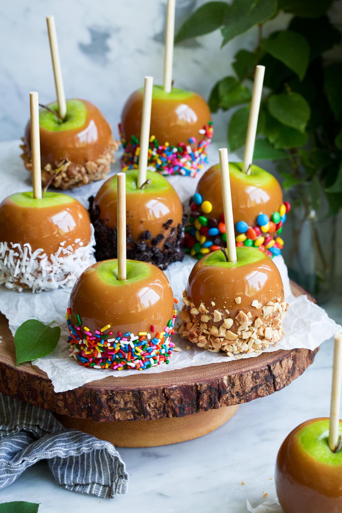 Easiest Caramel Apples! So tasty and so fun to decorate with all your favorite toppings! #caramelapples #apple #fall #recipe #dessert #caramel Caramel apples on a wooden cake stand. Apples are coated with various toppings.