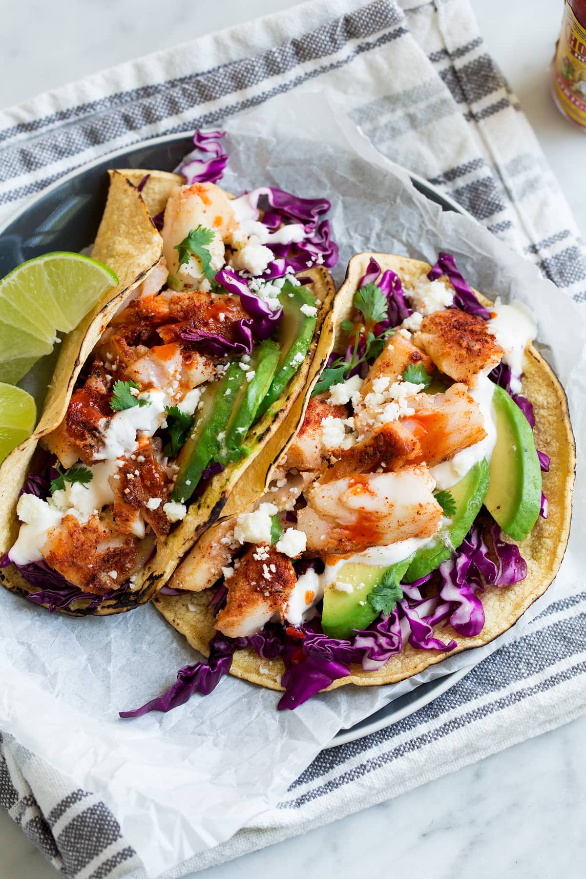 Fish Tacos - these are unbelievably delicious! Easy to make too! Includes directions for oven or grill - you'll love both, just don't omit the sauce! #fishtacos #tacos #fish #recipe Two fish tacos on parchment paper on a plate.