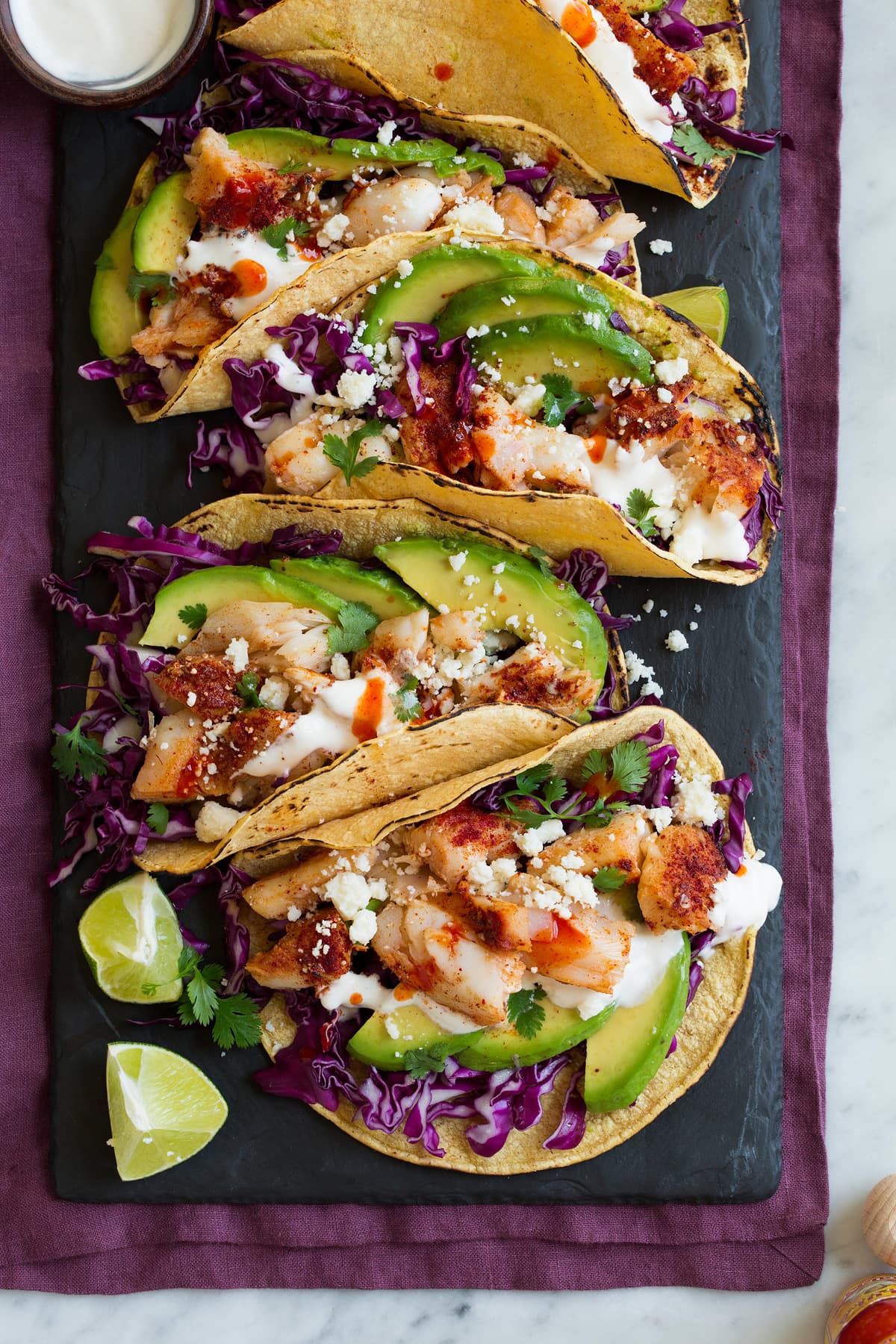 Fish Tacos - these are unbelievably delicious! Easy to make too! Includes directions for oven or grill - you'll love both, just don't omit the sauce! #fishtacos #tacos #fish #recipe Row of fish tacos on a black slate serving platter.