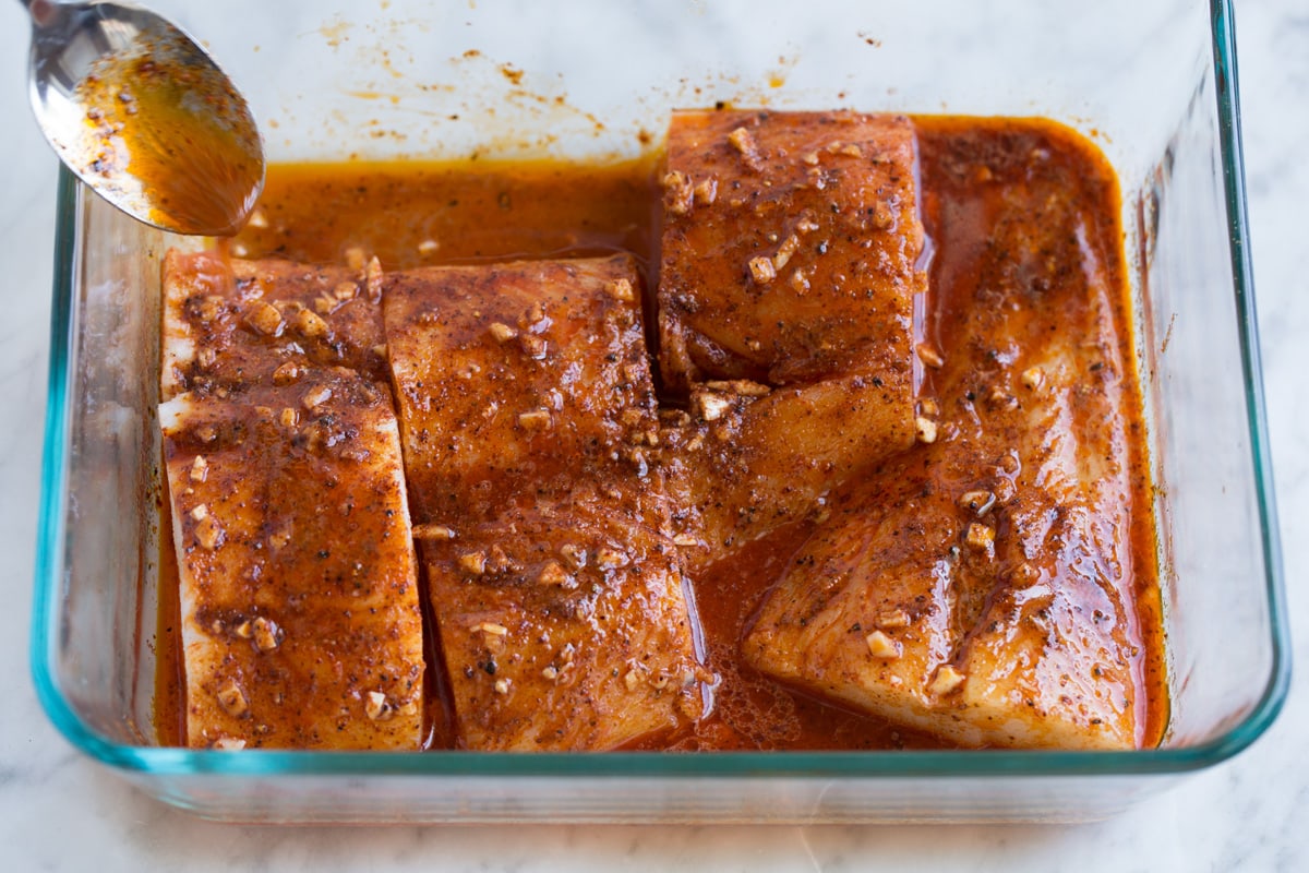 Fish Tacos - these are unbelievably delicious! Easy to make too! Includes directions for oven or grill - you'll love both, just don't omit the sauce! #fishtacos #tacos #fish #recipe Spooning marinade over fish in baking dish.