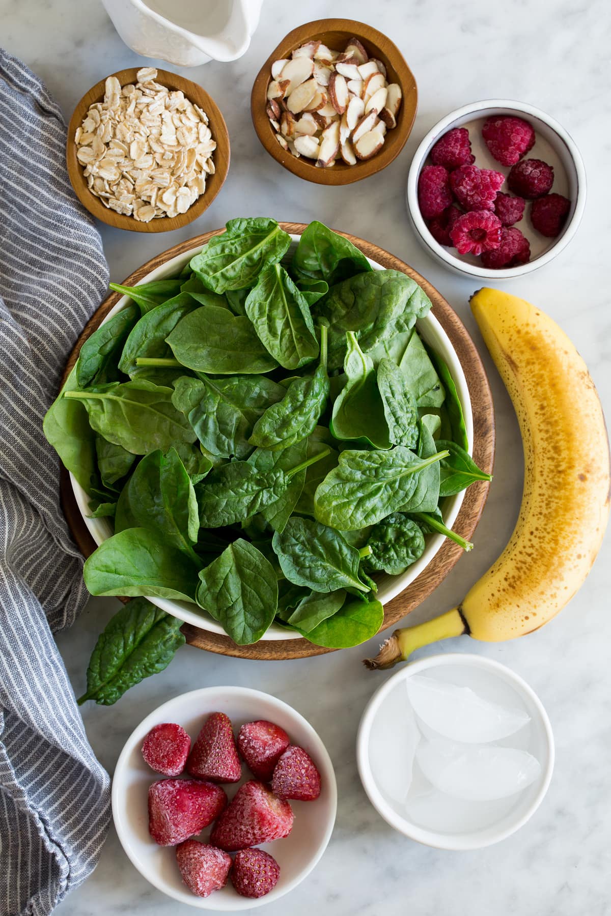 My go-to Green Smoothie! Healthy and perfectly filling. Made with spinach, berries, bananas, oats and almonds. #smoothie #greensmoothie #healthy #breakfast #smoothie Ingredients needed to make green smoothie shown here including spinach, strawberries, raspberries, bananas, almonds, oats, water, and ice.