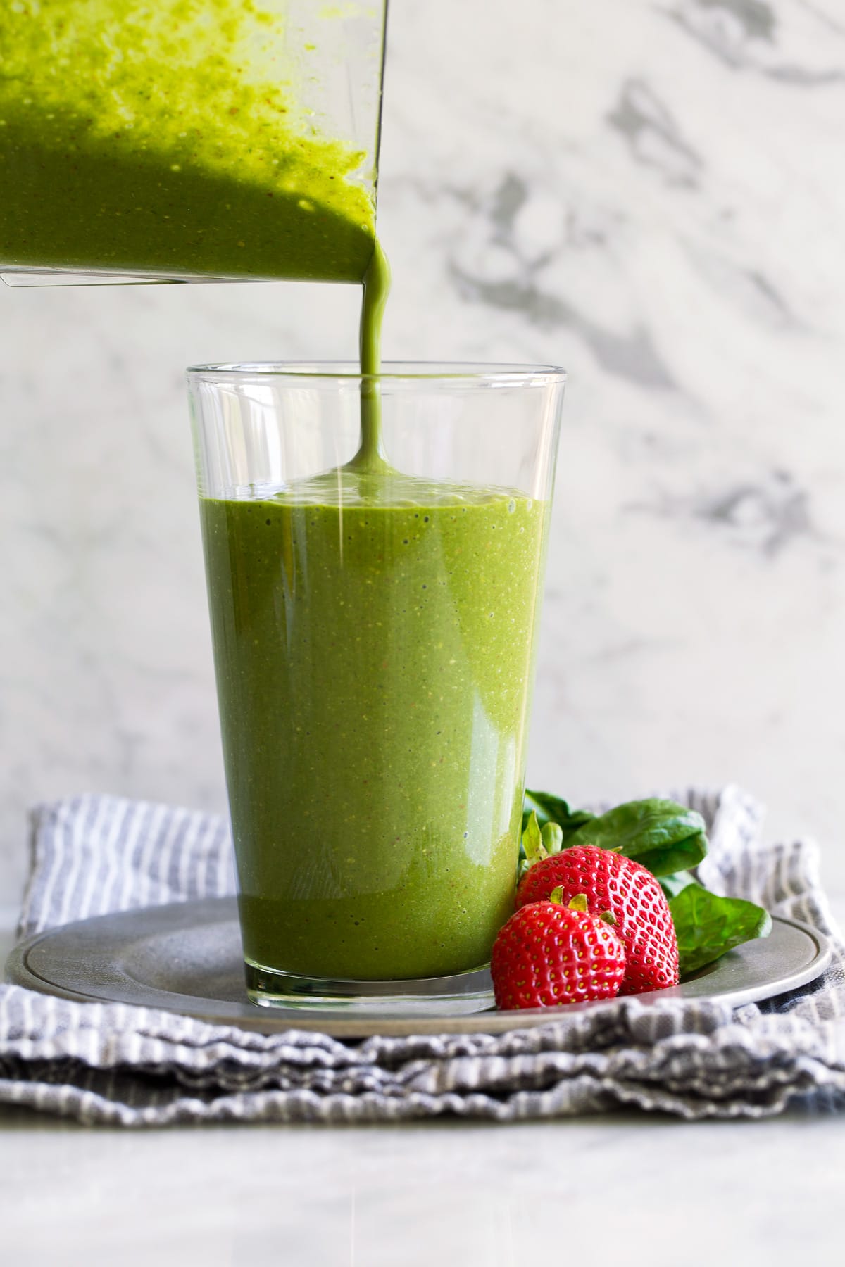 My go-to Green Smoothie! Healthy and perfectly filling. Made with spinach, berries, bananas, oats and almonds. #smoothie #greensmoothie #healthy #breakfast #smoothie Pouring green smoothie into a glass from a blender jar.
