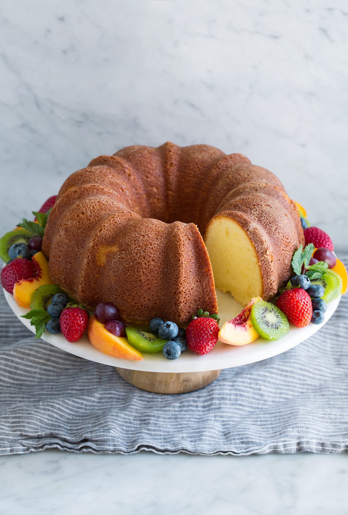 Pound Cake Pound cake with one sliced removed on a cake stand garnished with a ring of fresh fruit around the edges.