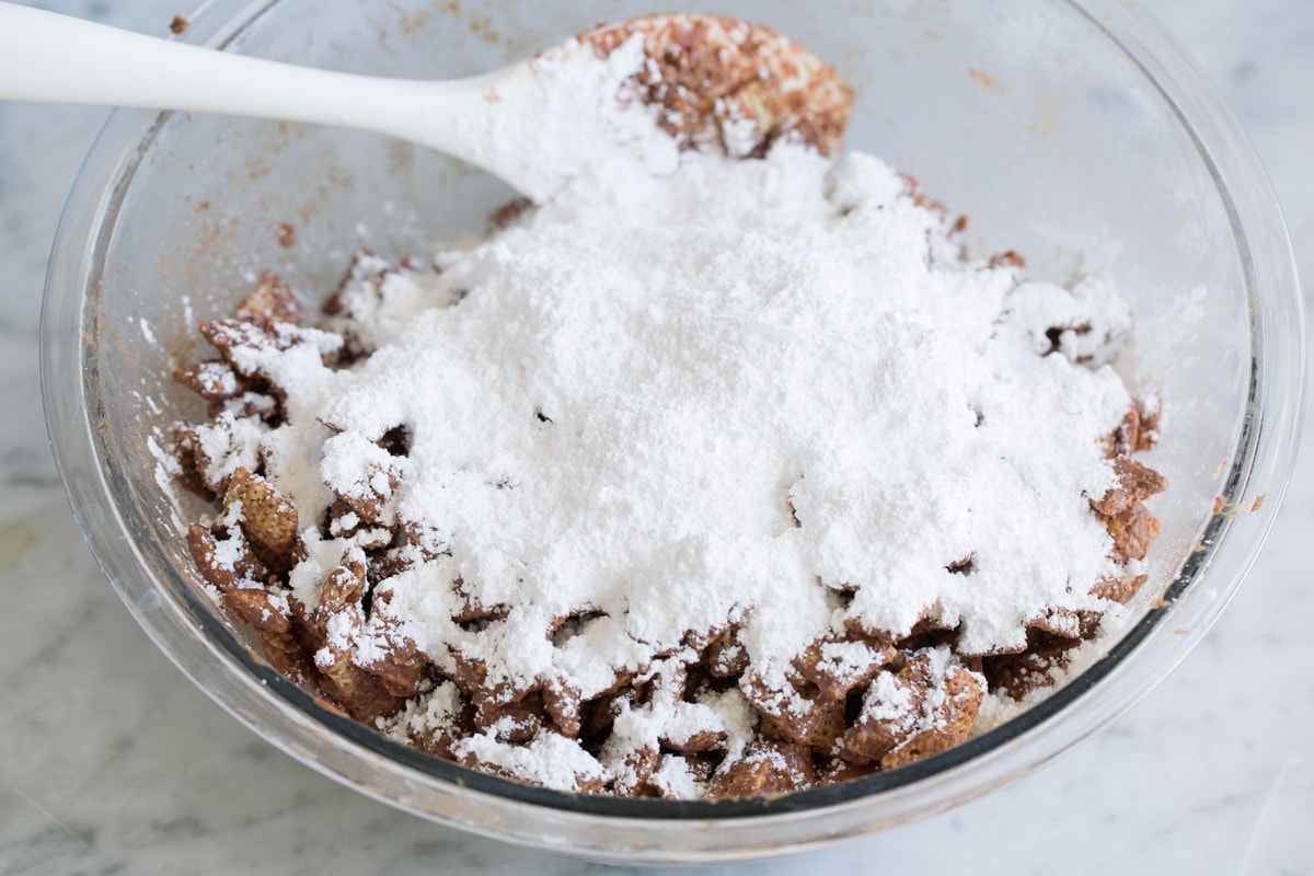 Perfect Puppy Chow {Muddy Buddies}! - one of my go-to treats! These are dangerously addictive! Perfect for parties, holidays and traveling too. #muddybuddies #puppychow #treat #chocolate #chex #peanutbutter Adding powdered sugar to puppy chow mixture.
