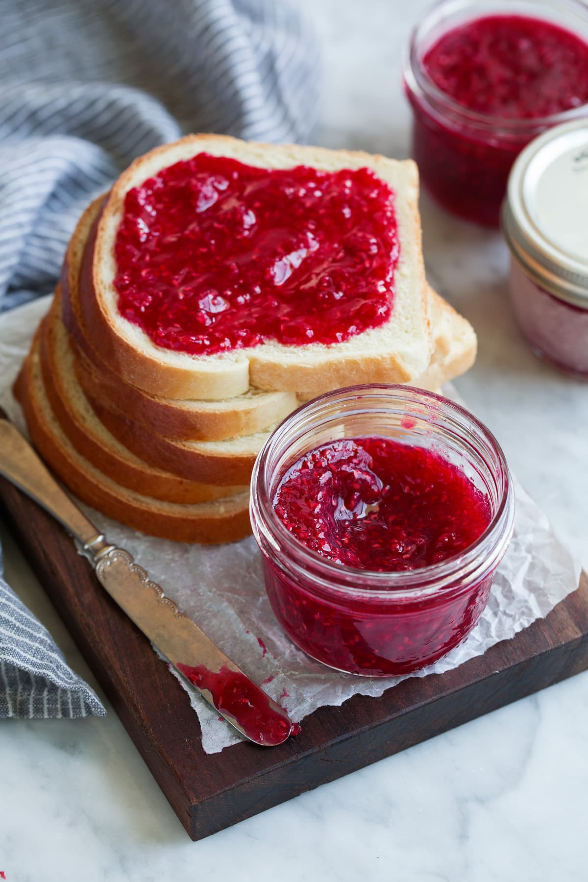 Easy Homemade Raspberry Freezer Jam - no canning skills or equipment required! This is my all time favorite jam! I've been making it for 10+years, it's the only jam I make now. Everyone always loves it and it freezes for up to 1 year! #jam #freezerjam #homeamdejam #easyrecipe Homemade jam in a jar next to a stack of bread with top slice slathered in jam.