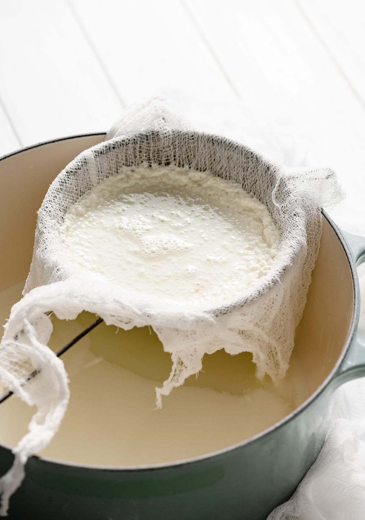 Homemade Ricotta Cheese - the BEST ricotta you'll try! It's so much better than store bought and incredibly easy to make! It's delicious in savory and sweet dishes and you can use the leftovers for toast. #ricotta #cheese #recipe #homemade #italianrecipes Ricotta cheese curds straining in a fine mesh sieve lined with cheese cloth. Sieve is resting over a large pot to drain.