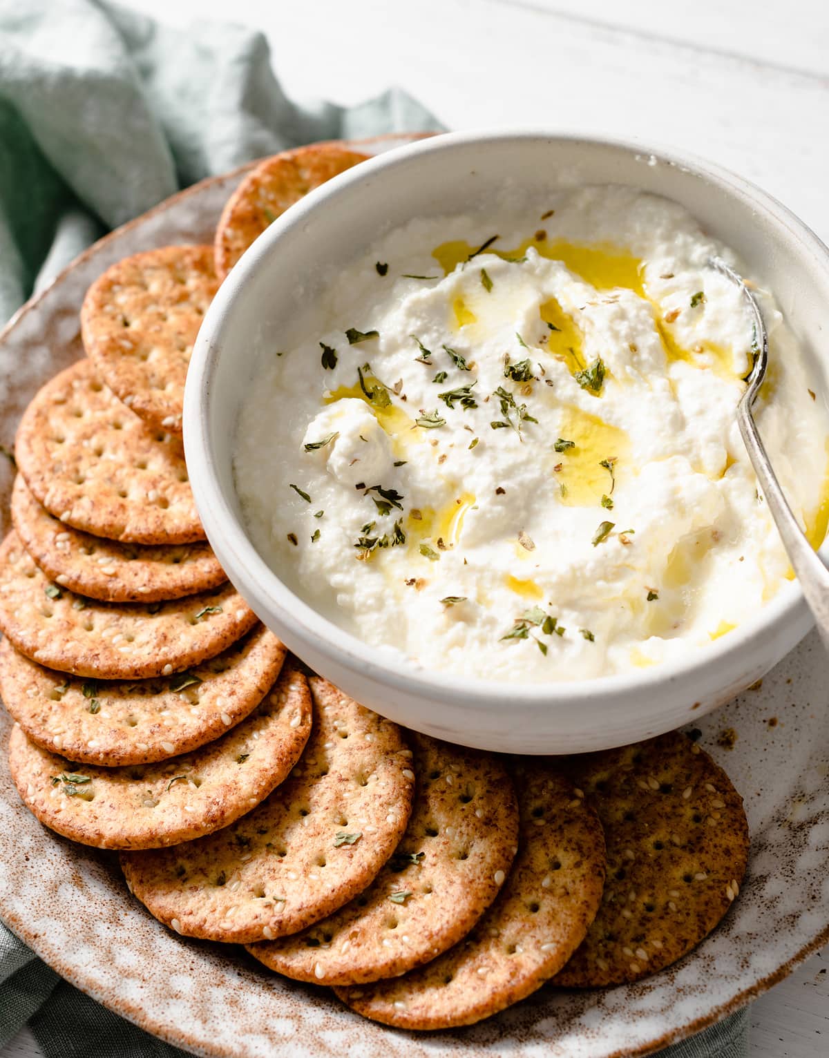 Homemade Ricotta Cheese - the BEST ricotta you'll try! It's so much better than store bought and incredibly easy to make! It's delicious in savory and sweet dishes and you can use the leftovers for toast. #ricotta #cheese #recipe #homemade #italianrecipes Homemade ricotta in a serving bowl drizzled with olive oil, sprinkles with dried herbs and served with a side of crackers.