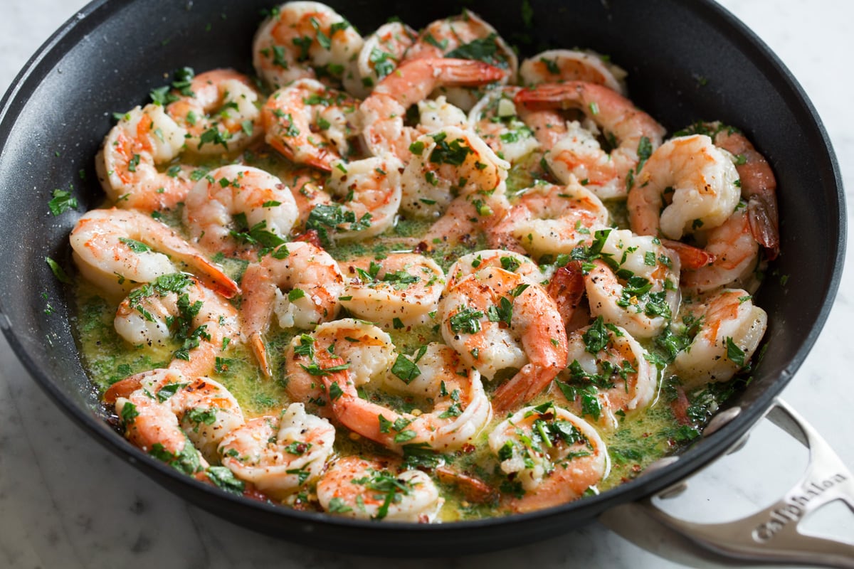 Shrimp Scampi - shrimp are seared in an incredibly flavorful buttery wine sauce and tossed with pasta for the perfect, unforgettable dinner! Everyone will go crazy over this! #shrimp #scampi #pasta #garlic #dinner #recipe Herbs added to shrimp scampi in skillet.