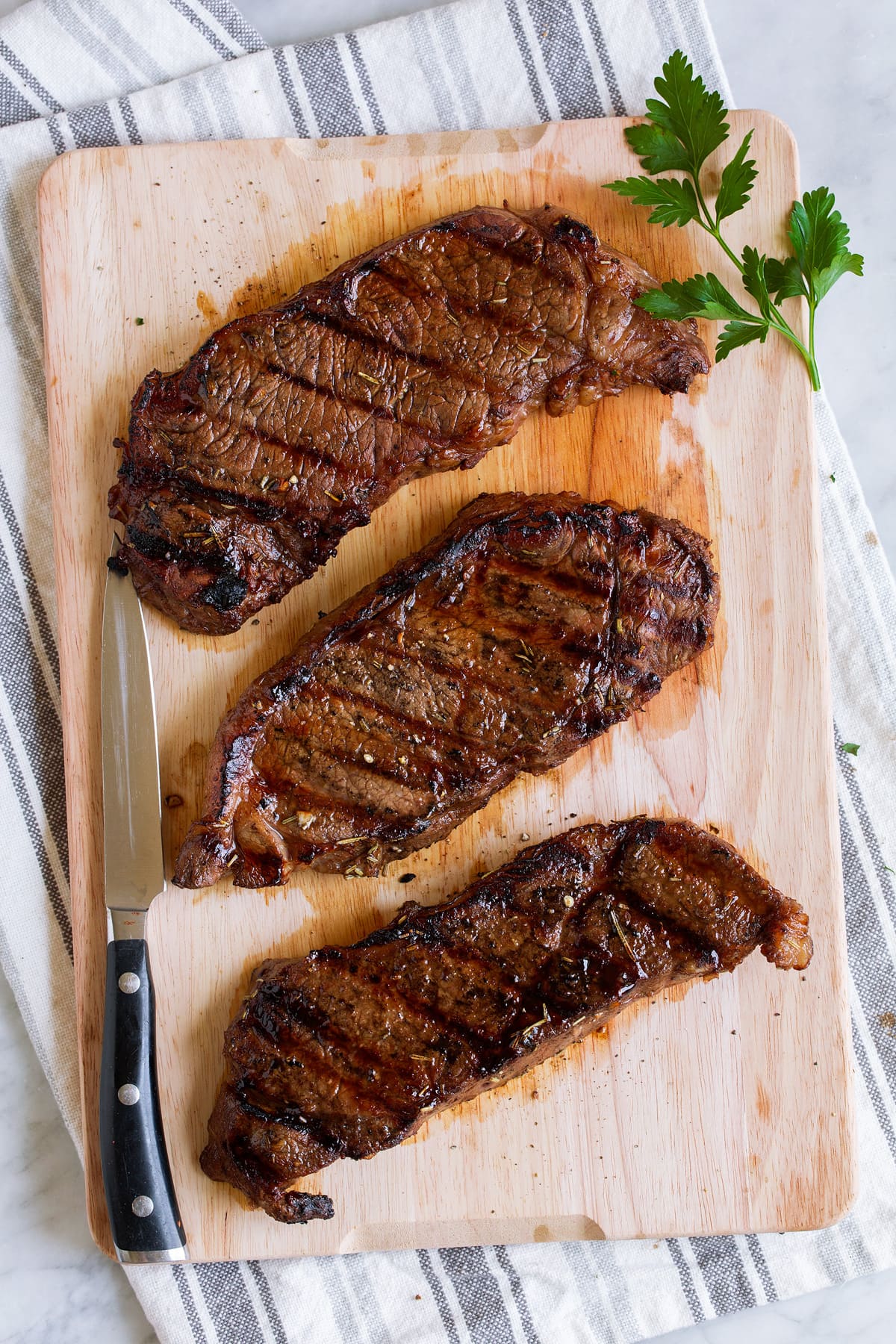 The BEST Steak Marinade! Made with balsamic vinegar and a handful of other pantry staples. A summer must have recipe! #steak #marinade Three steaks on a wooden cutting board.