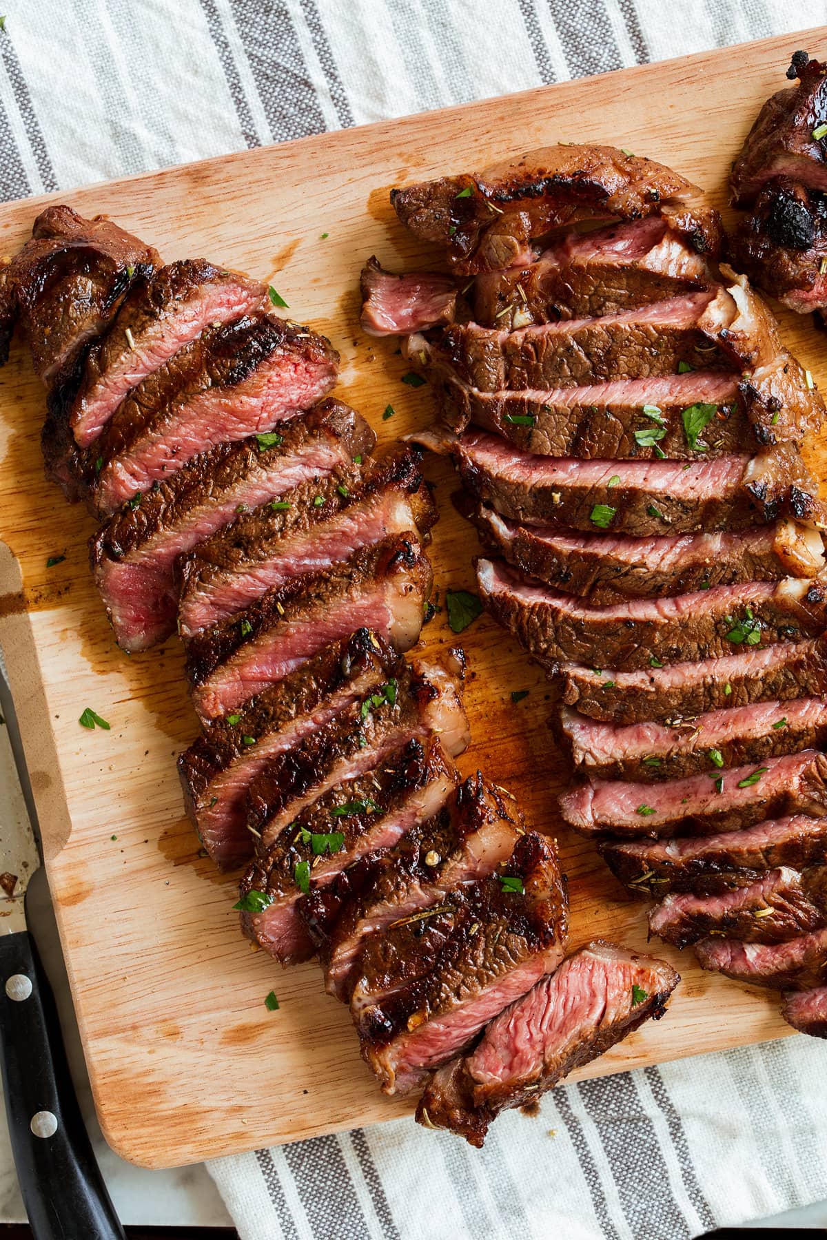 The BEST Steak Marinade! Made with balsamic vinegar and a handful of other pantry staples. A summer must have recipe! #steak #marinade Two sliced new york strip steaks on a wooden cutting board.