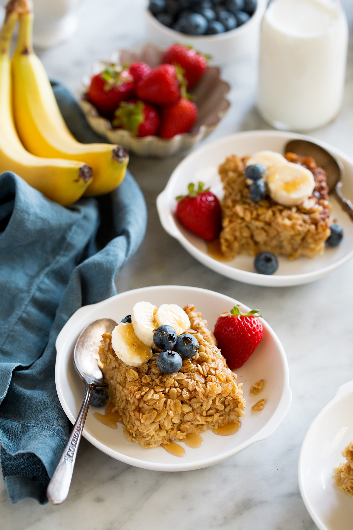 Baked Oatmeal Squares of baked oatmeal topped with fresh fruit in white serving bowls.