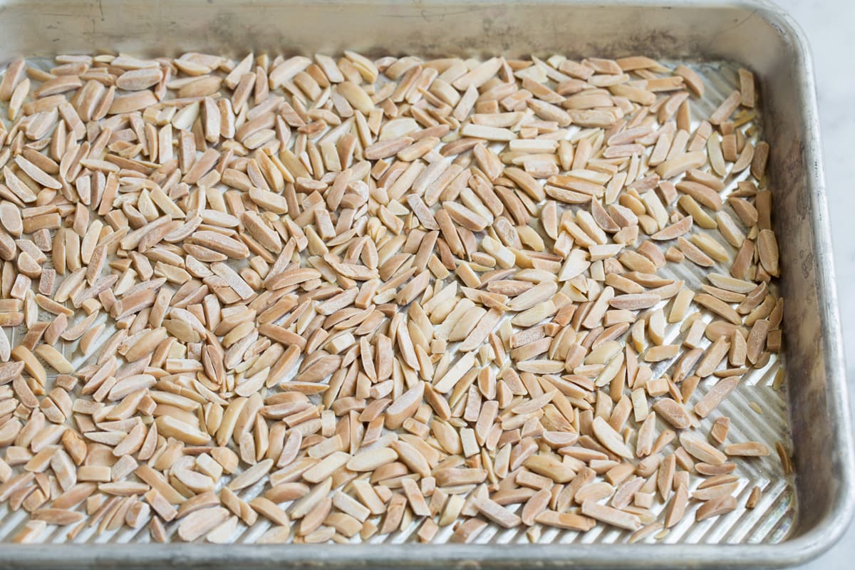 Perfect Broccoli Salad! A classic must have recipe! Made with crisp pieces of tiny broccoli florets, salty bacon, sweet dried cranberries, bright red onion, nutty toasted almonds and a creamy rich dressing. #broccoli #salad #summer #sidedish #recipe Toasted slivered almonds on a baking sheet.