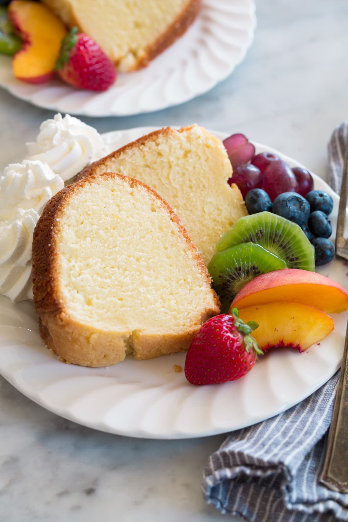 Pound Cake Slice of pound cake on a dessert plate with a side of fresh fruit and whipped cream.
