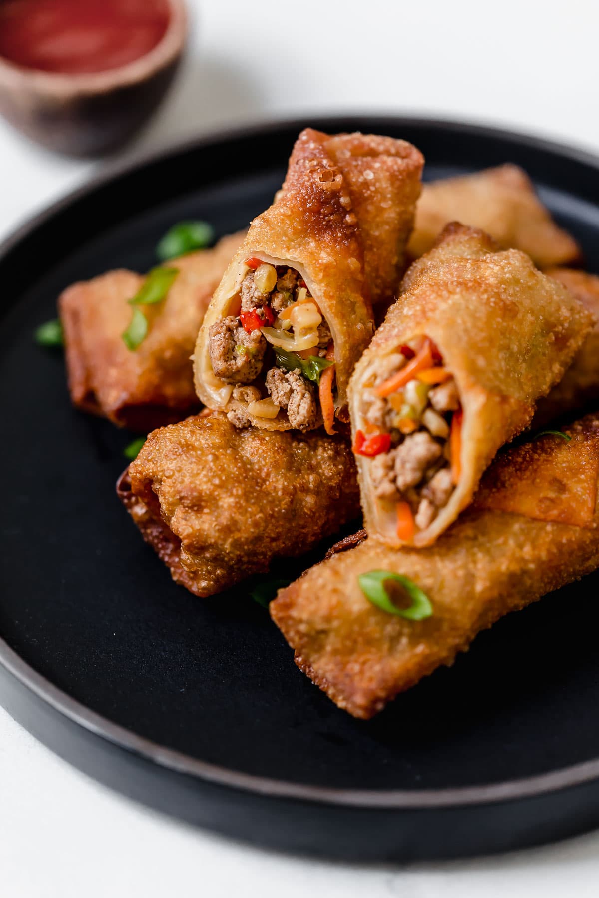 Egg Rolls {Fried or Baked} Egg rolls stacked on a black plate with one cut in half to show exterior.