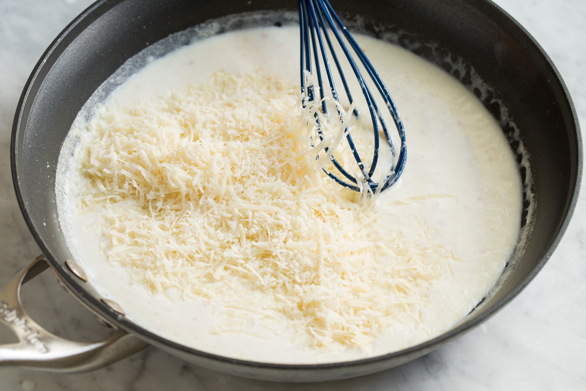 Best Alfredo Sauce - made with half milk and half cream so it's not too heavy, and includes plenty of parmesan for incredible flavor! So easy and seriously delicious! #alfredosauce #alfredo #fettuccinealfredo #dinner #pasta Adding shredded parmesan to cream mixture in skillet.