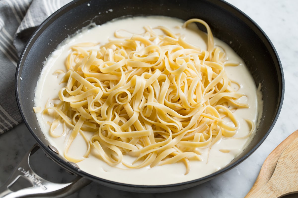 Best Alfredo Sauce - made with half milk and half cream so it's not too heavy, and includes plenty of parmesan for incredible flavor! So easy and seriously delicious! #alfredosauce #alfredo #fettuccinealfredo #dinner #pasta Cooked fettuccine pasta over alfredo sauce in skillet before tossing.