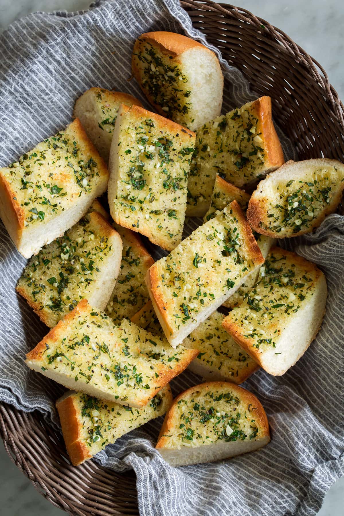 Garlic Bread - super fast, super easy and incredibly flavorful! Skip the margarine coated garlic bread from the store and make this butter version instead, it's a hundred times better! #garlicbread #sidedish #bread #appetizer Garlic bread slices in a basket with a kitchen cloth.