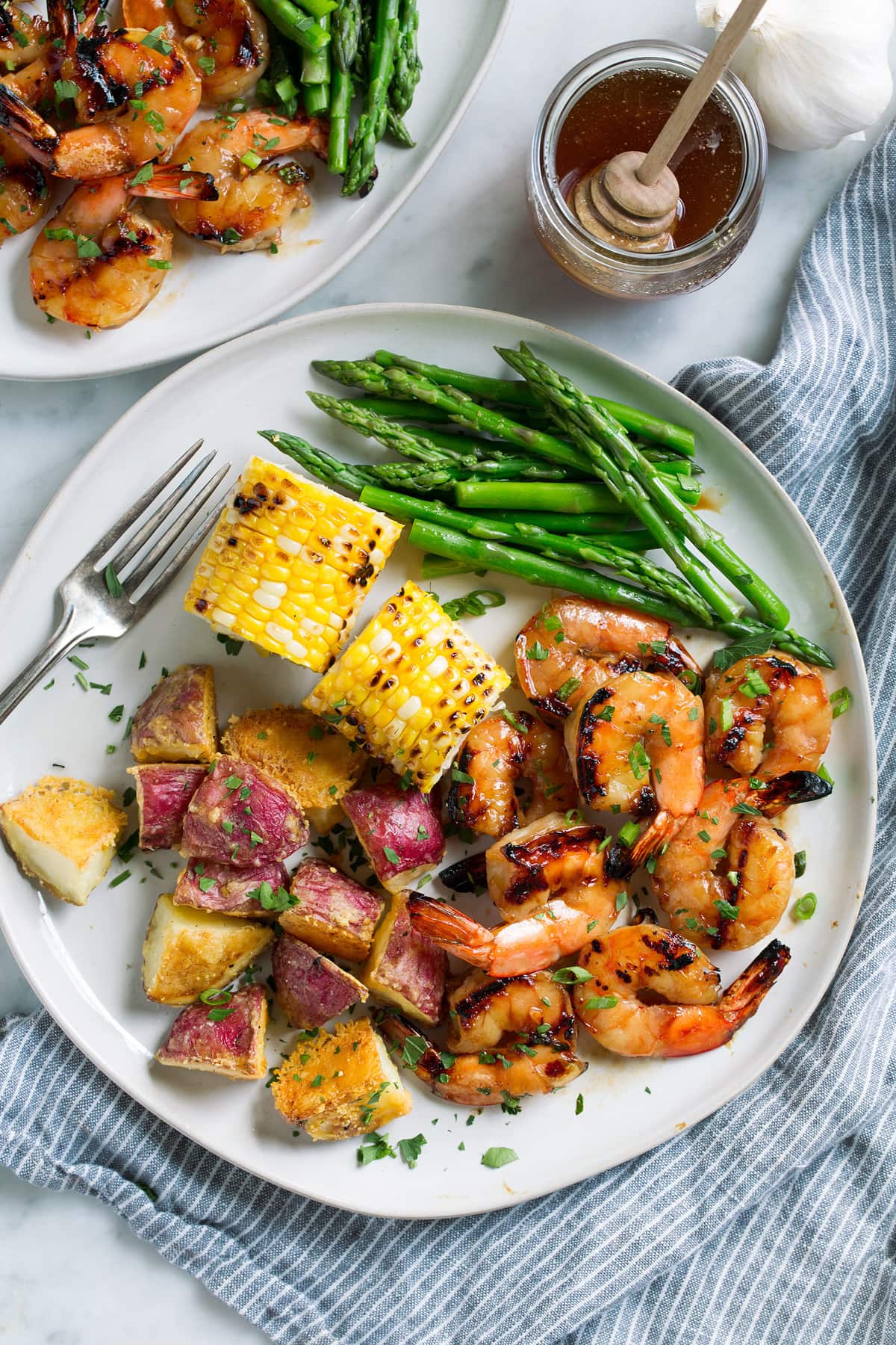 Grilled Shrimp with Honey Garlic Marinade - only 4 ingredients in this fast, easy and flavorful marinade! Perfect for a quick dinner! #shrimp #marinade #grilledshrimp #dinner #recipe Grilled shrimp on a plate with a side of grilled corn, steamed asparagus and roasted potatoes.