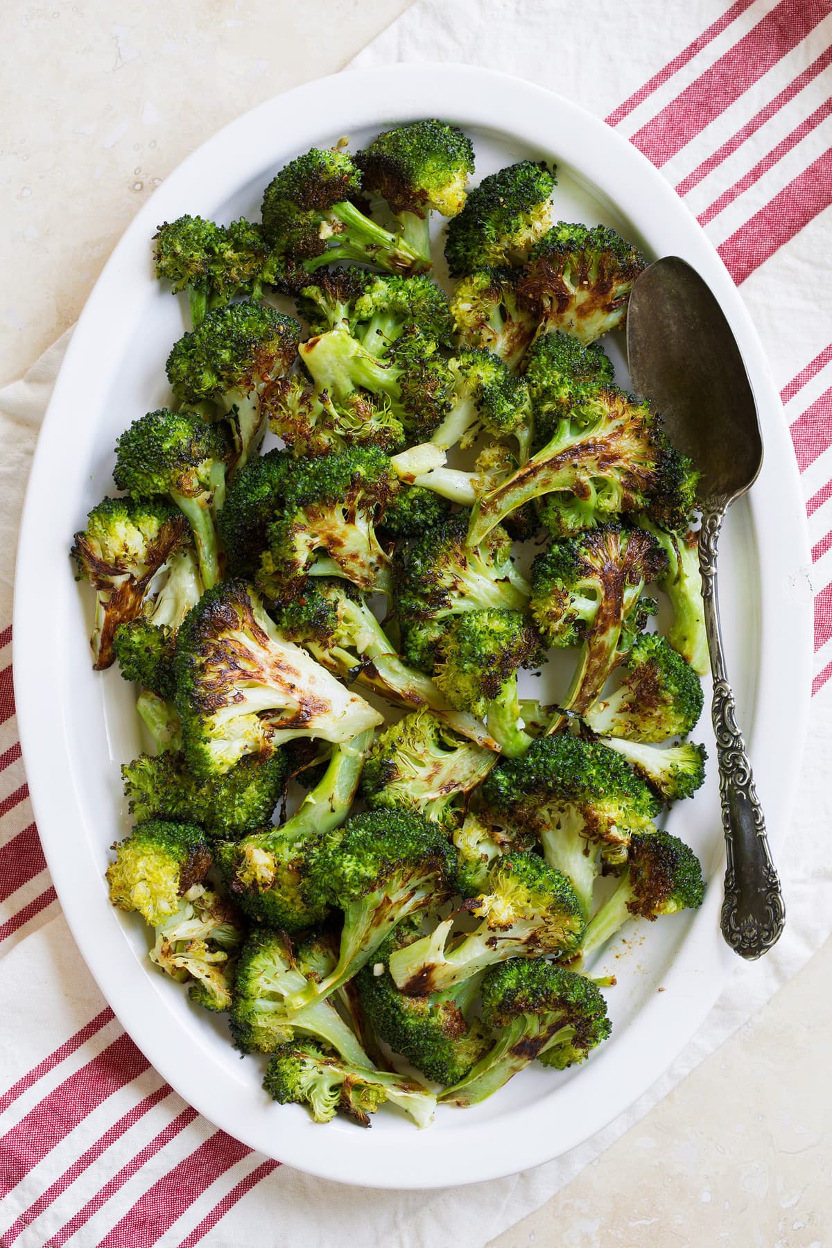 Roasted broccoli on an oval white platter with a serving spoon.