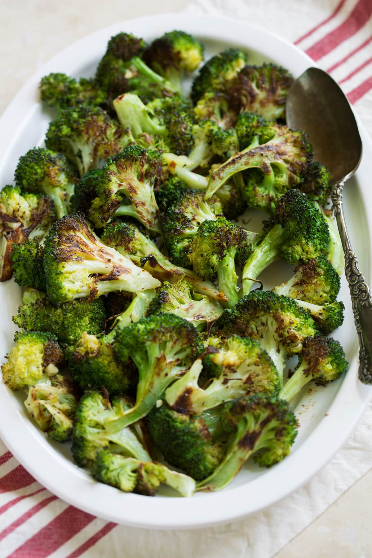 perfectly tender, deliciously browned and incredibly flavor. Broccoli goes from drab and bland to perfectly flavorful with this simple method. The best way to cook broccoli! Broccoli on a serving plater over a striped napkin and beige table surface.