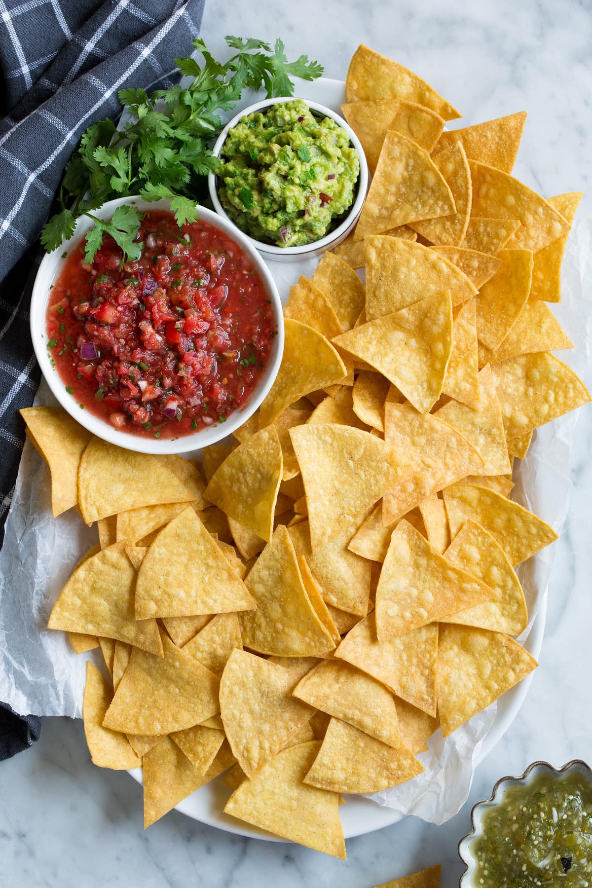 Homemade Tortilla Chips Platter full of homemade tortilla chips with a side of salsa, guacamole and salsa verde.