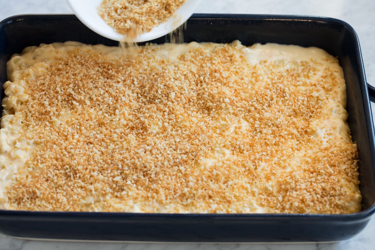 Baked Macaroni and Cheese Pouring panko topping over macaroni and cheese in baking dish.