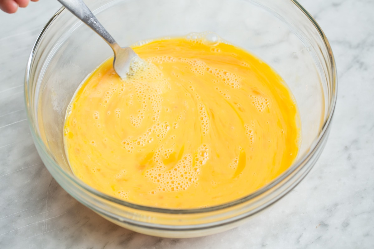 Breakfast Casserole Whisking eggs with a fork in a glass bowl.