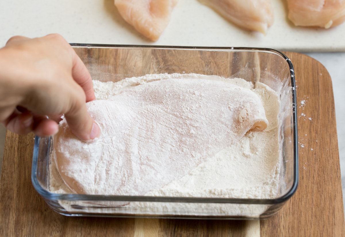 Chicken Piccata Dredging a chicken cutlet in flour in a glass dish.