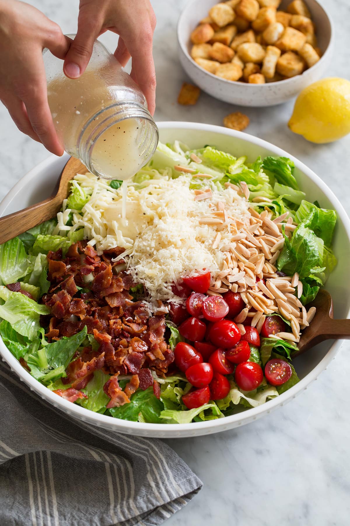 The BEST Salad Recipe {Salad de Maison} Pouring lemon dressing over Family Favorite salad in a large white bowl.