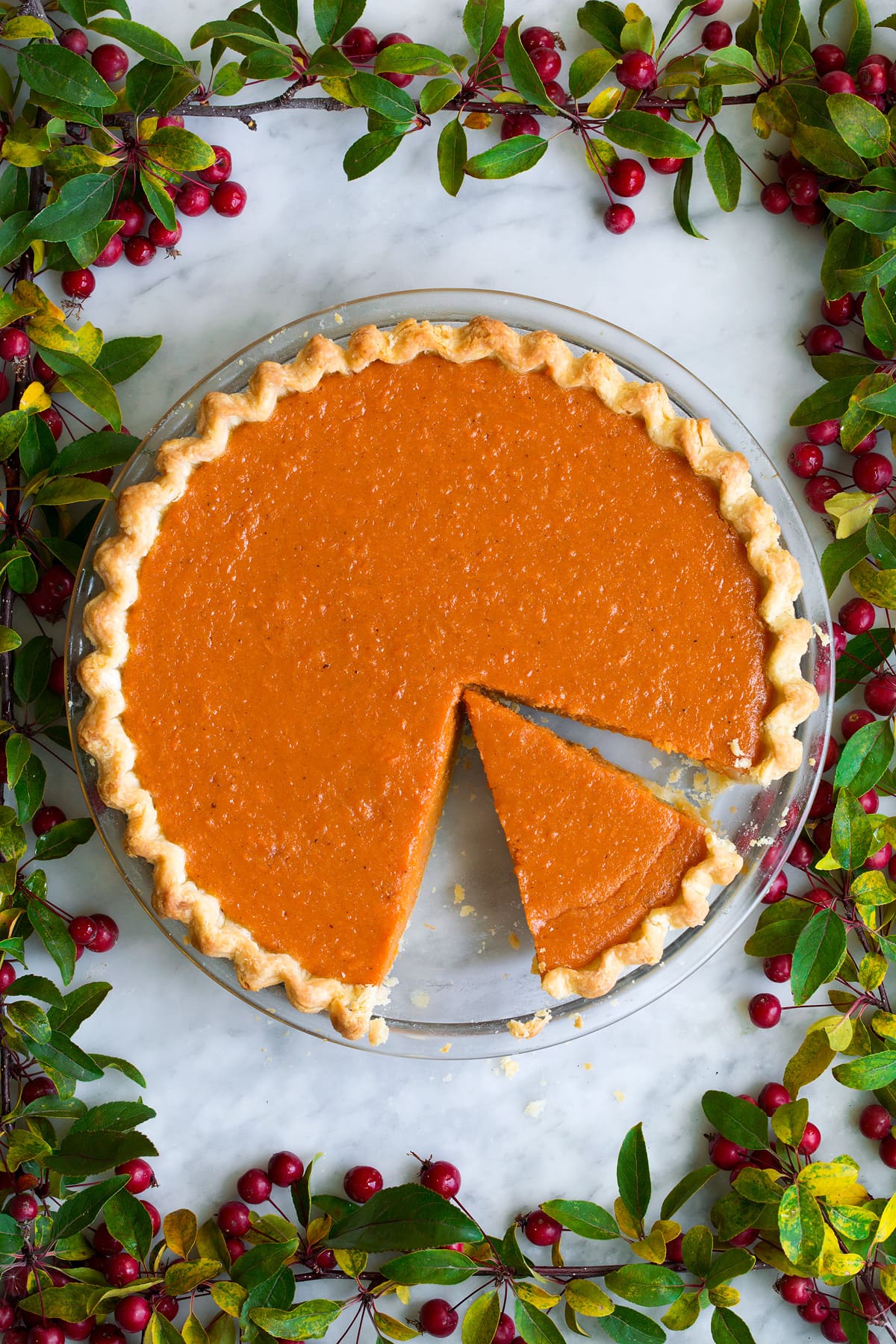 Perfect Sweet Potato Pie Sweet potato pie with one sliced cut. It's decorated with berry tree branches around it.
