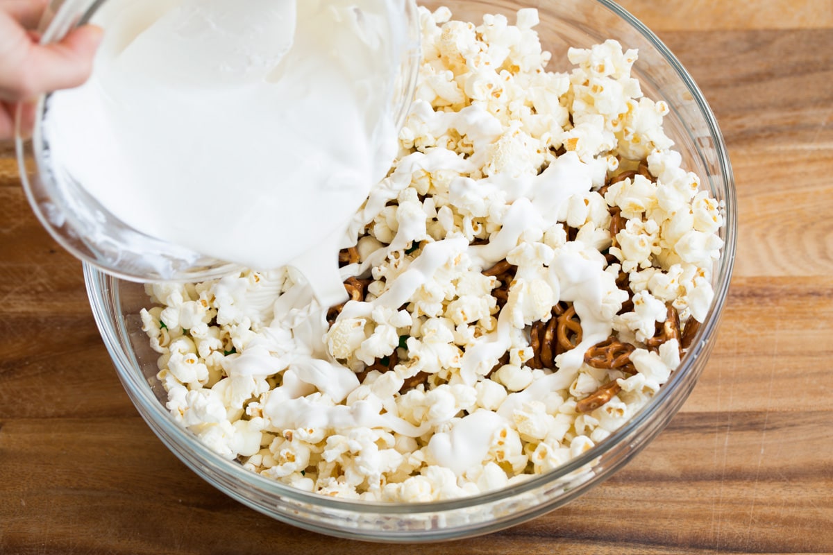 Christmas Crunch Pouring melted white chocolate candy coating over popcorn.