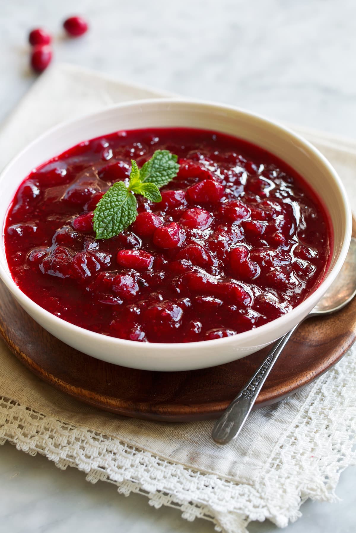 Cranberry Sauce - this has an amazing fresh flavor, it's 100x better than the jelly like stuff that comes in a can! Plus it's super easy to make! A Thanksgiving staple every year! #cranberrysauce #thanksgiving #sidedish #recipe Cranberry Sauce in a serving bowl set over a wooden platter. Sauce garnished with fresh mint.
