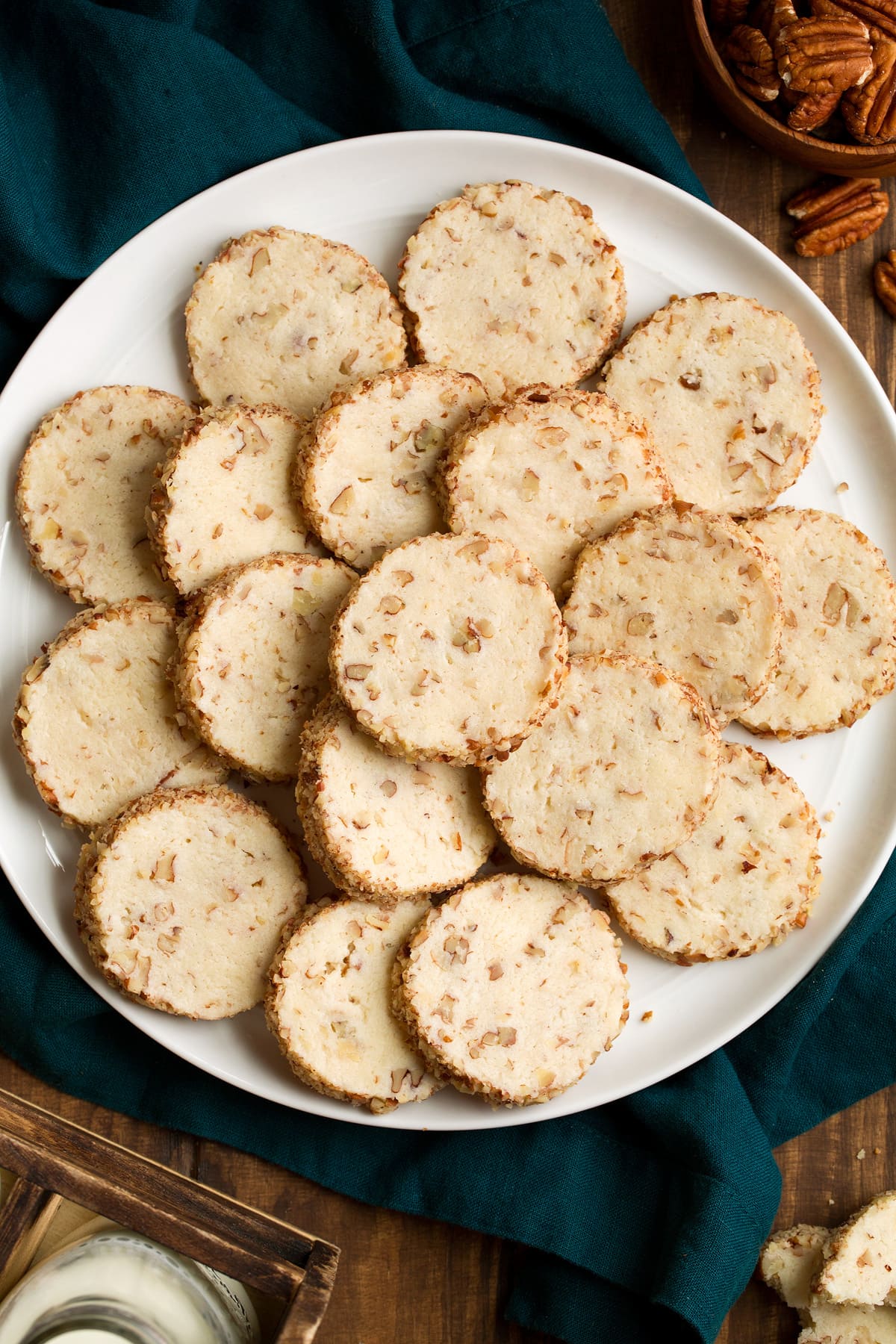 Cream Cheese Pecan Cookies Overhead image of cream cheese pecan cookies stacked on a white serving plate set over a blue cloth.