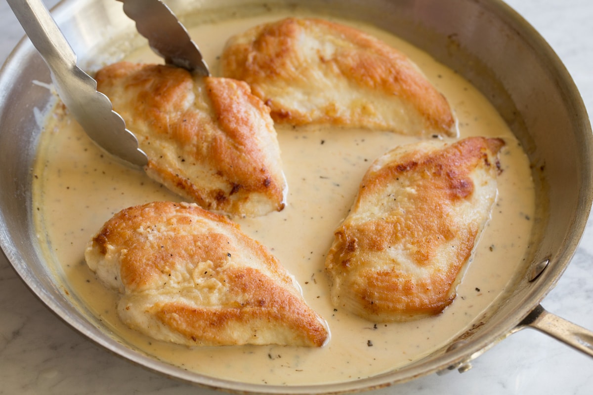 Creamy Lemon Romano Chicken Placing chicken breasts into sauce mixture in pan with tongs.