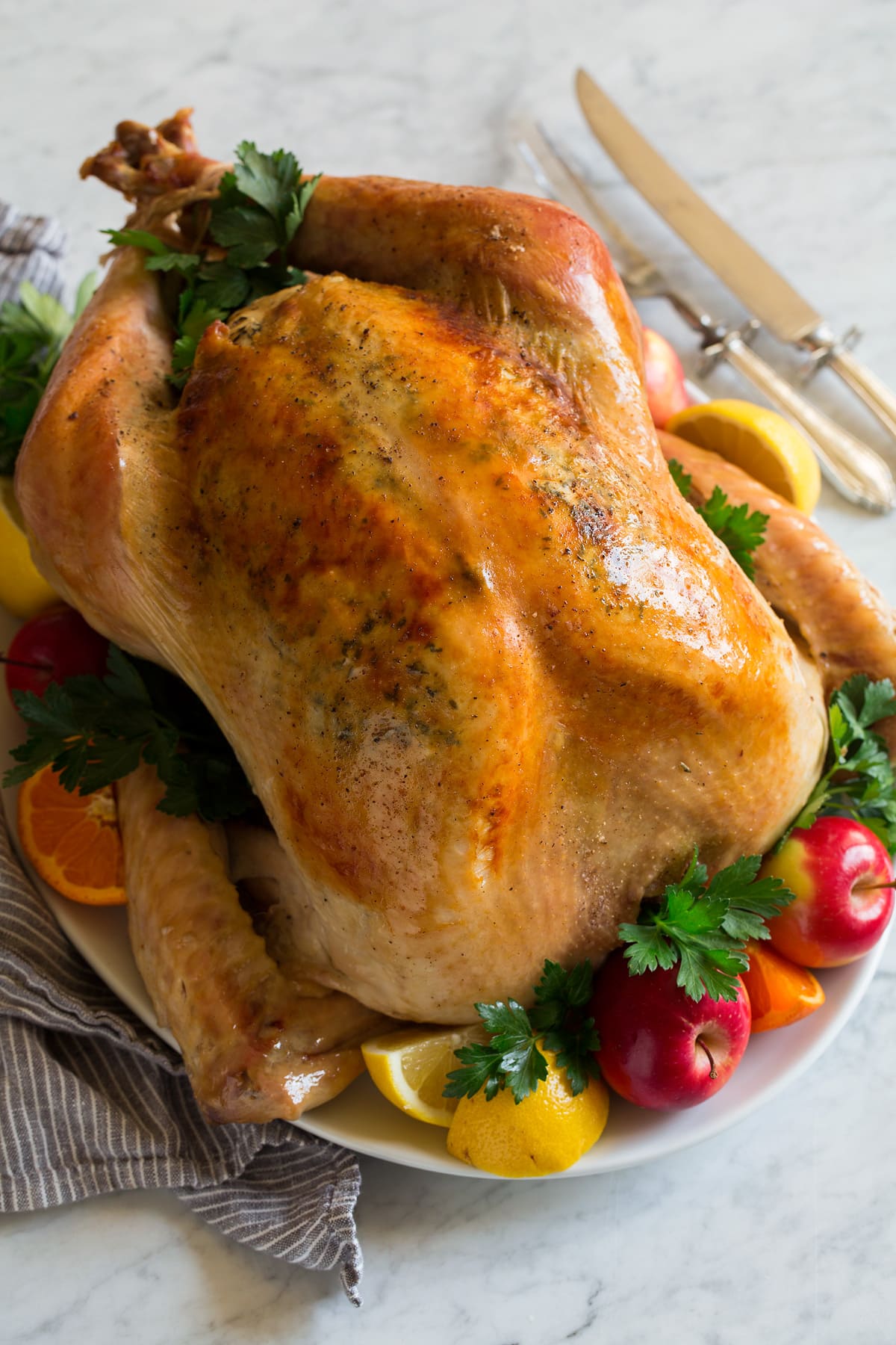 How to Cook a Juicy and Tender Turkey Turkey on a serving platter with fruit and fresh herbs.