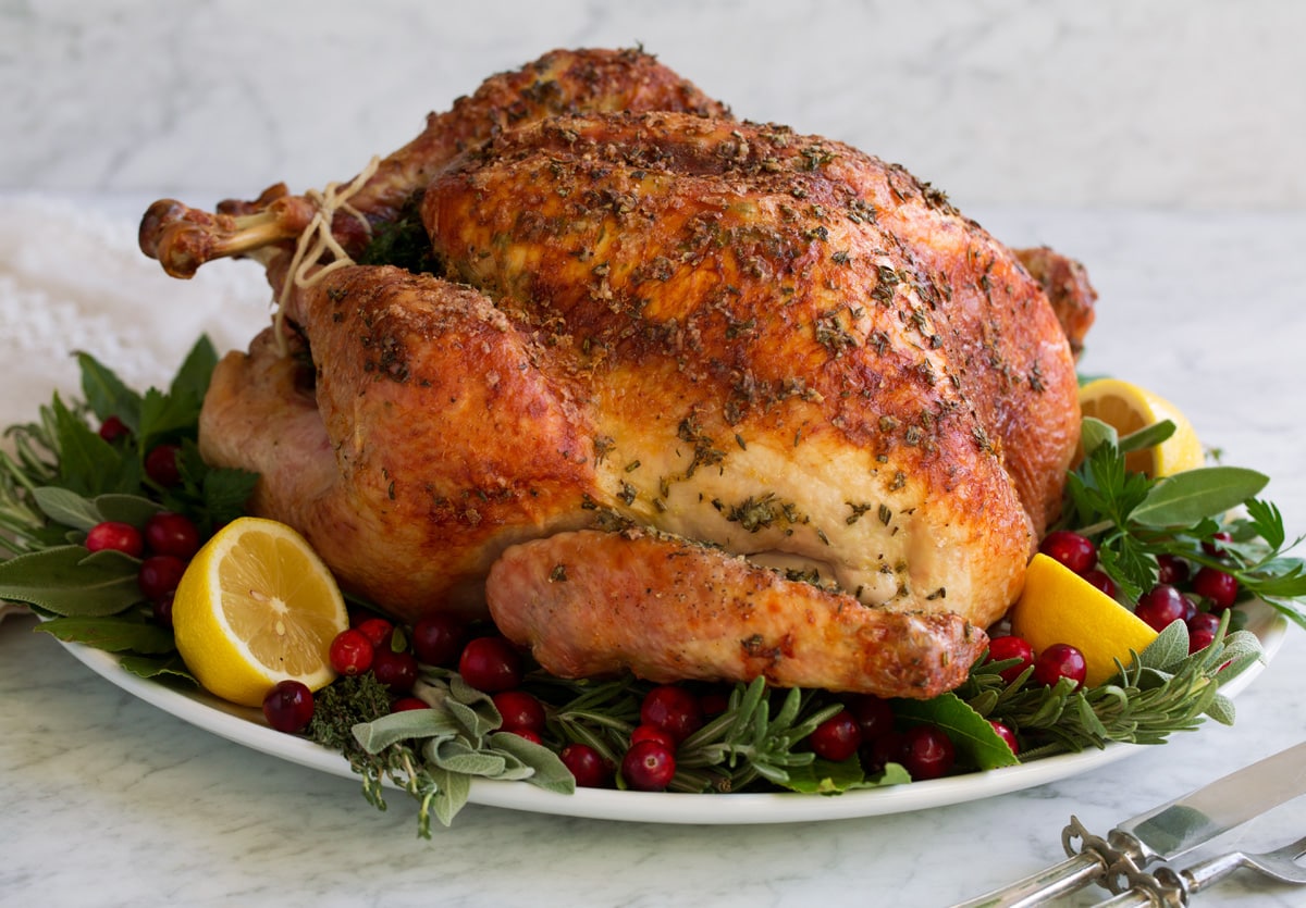 Roast Turkey - easy to follow recipe that turns out tender, juicy and full of flavor! A holiday staple! #turkey #thanksigiving Whole roasted turkey on a serving platter with herbs lemons and cranberries