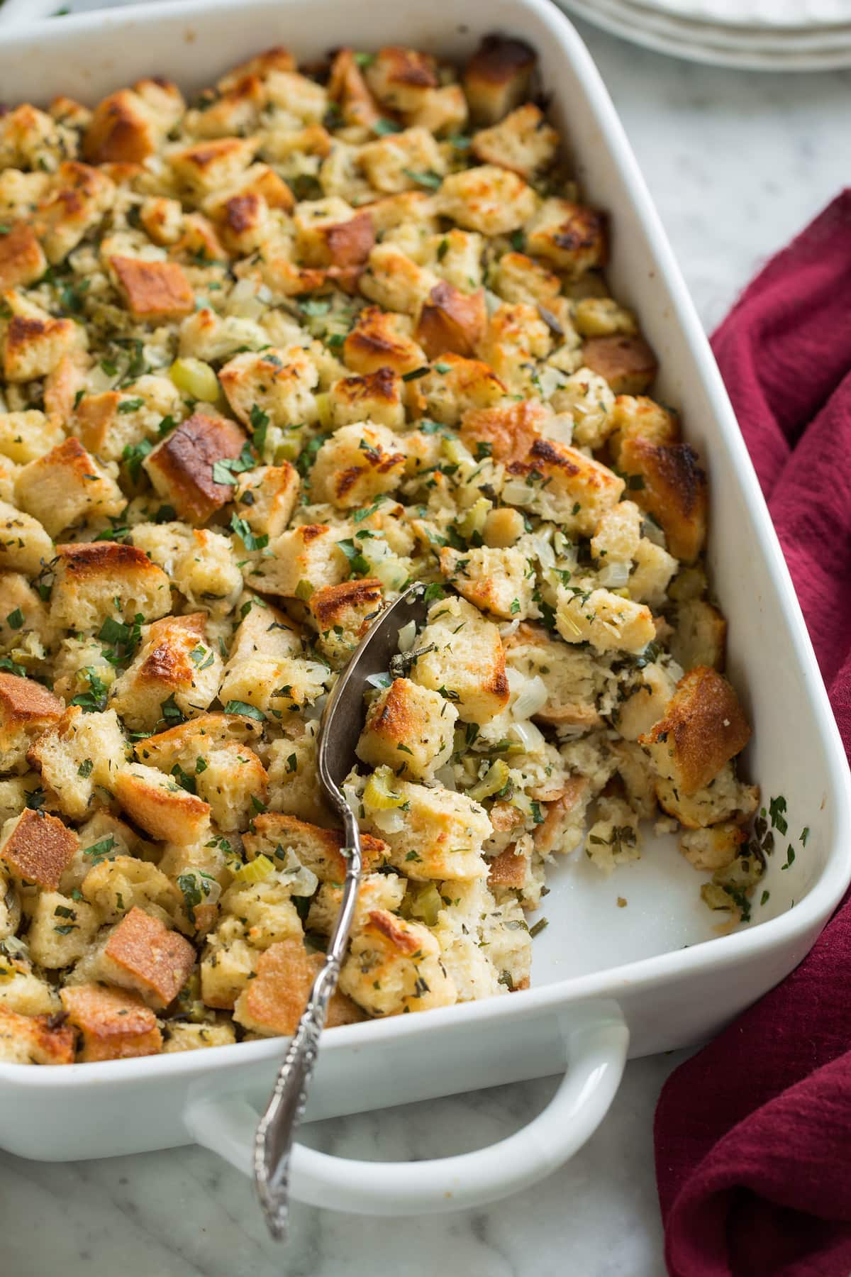 Stuffing Recipe - this is my FAVORITE stuffing! It's perfectly moistened in the center, browned and crisp on the edges and packed with butter and herb flavor. A fall staple! #stuffing #thanksgiving #sidedish #recipe Scooping out a spoonful of stuffing in baking dish.